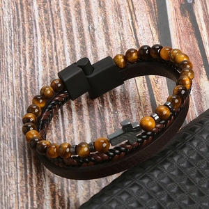 Detail of multi-layer braided leather bracelet with tiger eye beads and metal cross on wood