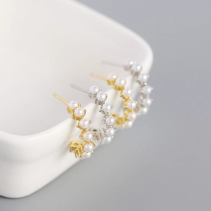 Detailed view of silver and gold C-shaped hoop earrings with pearls on a ceramic dish
