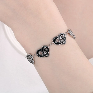 Detail of silver heart link bracelet with black enamel outlines on a model wrist