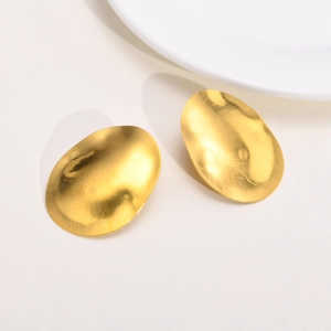 Minimalist golden oval brushed metal stud earrings on a clean white ceramic dish