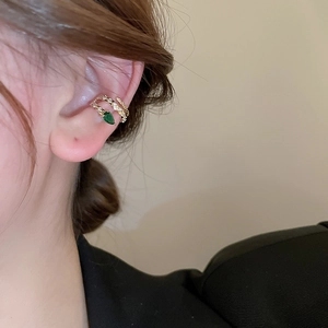 Detailed close-up of a twisted gold ear cuff featuring a teardrop green gemstone on model