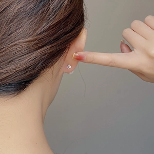 Close-up of minimalist mini silver sphere stud earring worn on ear showing glossy finish
