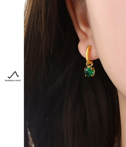 Primo piano di un orecchino in acciaio inossidabile dorato con uno zircone verde brillante
