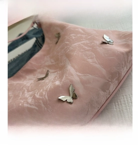 Close-up of pink wrinkled tote bag featuring decorative silver metal butterfly ornaments