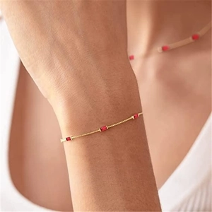 Close-up of minimalist gold chain bracelet featuring three rectangular red gemstones