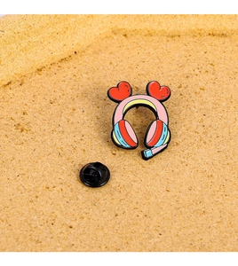 Close-up of pink game console headphone enamel pin with red heart on cork background