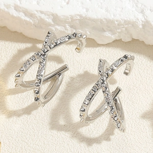 Macro detail of silver X-shaped zircon earrings with micro-inlaid stones on white stone