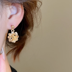 Detailed view of golden flower earrings with brushed metal texture and retro finish