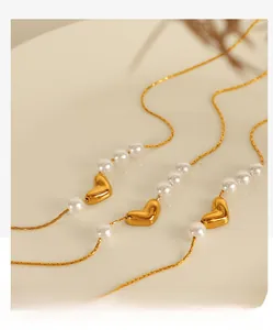 Détail de colliers avec pendentif cœur en or et perles blanches sur un fond minimaliste