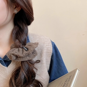 Close-up of brown knit scrunchie with fashion label on model ponytail against beige wall