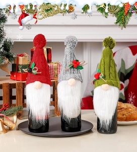 Three knitted Christmas gnome wine bottle covers in red, grey, and green colors