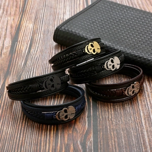 Handwoven leather bracelet set featuring metal skull charms on a rustic wooden background