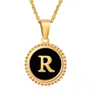 Macro shot of gold letter R pendant with black enamel inlay and beaded edge detail