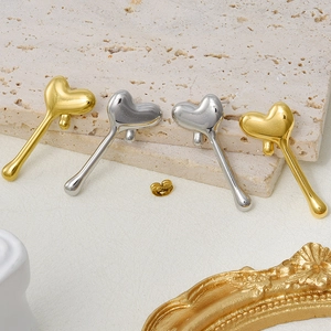 Detail of 18k gold and silver heart-shaped drop earrings on a textured stone surface