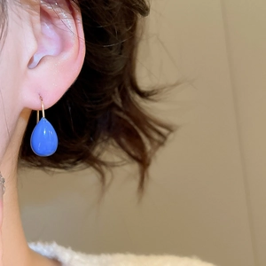 Gros plan de boucles d'oreilles gouttes bleues avec crochets dorés portées par un modèle