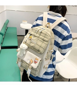 Detail of beige plaid canvas backpack featuring cute bear charm and cartoon badges