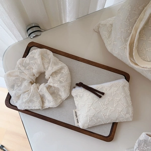 Detail of floral lace embroidery on a beige cotton scrunchie and zipper storage pouch