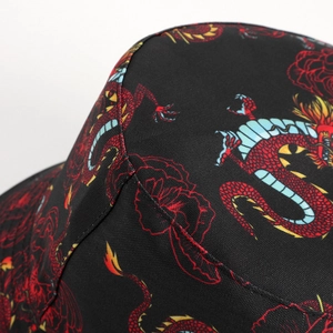 Dettaglio di un cappello da pescatore in tela nera con stampe di draghi rossi e fiori