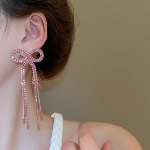 Close-up of elegant pink crystal bow earrings with long tassels on a model