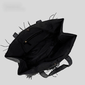 Black woven straw tote bag with tassels showing inner lining and zipper pocket
