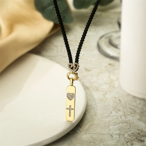 Pendentif doré avec cœur et croix en diamant sur cordon noir posé sur une assiette