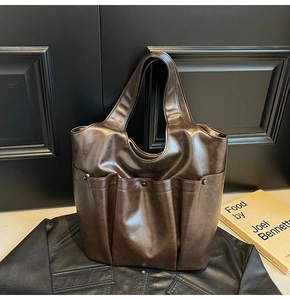 Brown leather tote bag featuring front pockets and large capacity on black leather jacket