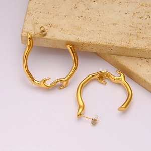 Détail macro de boucles d'oreilles dorées en acier inoxydable au design abstrait