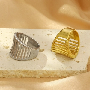 Polished 18K gold and silver hollowed-out stainless steel wide rings on stone surface