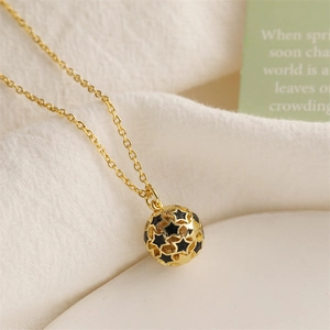 Macro shot of gold hollow ball pendant with black enamel stars on a dainty chain