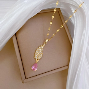 Close-up of gold angel wing necklace with pink teardrop crystal on jewelry box