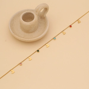 Detail of gold heart necklace with colorful gemstone charms on a minimalist beige background
