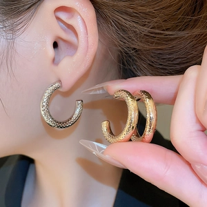 Macro detail of C-shaped hoop earrings with textured hammered finish in gold and silver
