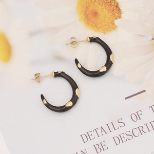 Detail of C-shaped black enamel earrings with liquid gold accents on floral background
