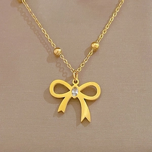 Macro detail of gold-plated titanium necklace featuring a sparkling zircon bow pendant