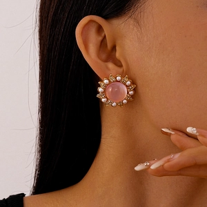 Close-up of pink flower stud earring with pearls and rhinestones on woman's ear