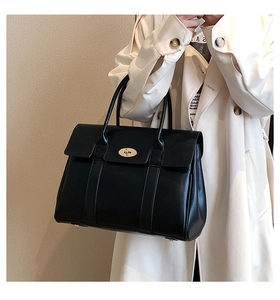 Detail of the iconic gold oval twist lock on a black leather tote bag worn by a model