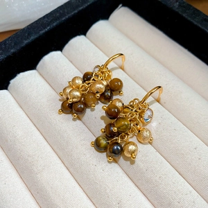 Detail of golden tassel earrings with brown tiger eye beads and zircon stones on a soft tray