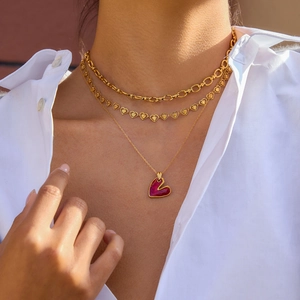 Dettaglio di collane a strati in acciaio dorato 18K con ciondolo a cuore rosso
