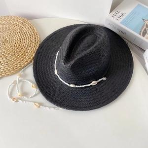 Detail of black woven straw sun hat featuring white shell band and beaded lanyard strap