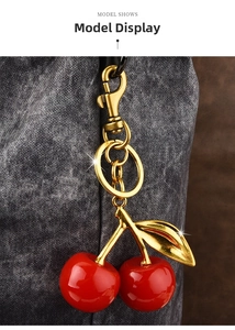 Close-up of red resin cherry charm with gold leaf hanging on a gray fabric handbag