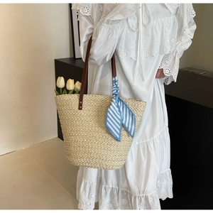 Detail of straw tote bag with brown leather straps and blue striped scarf accessory