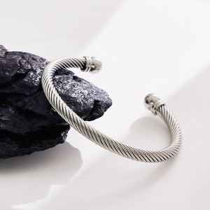 Detail view of a silver twisted steel wire cuff bracelet on a textured dark rock