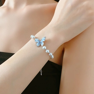 Détail d'un bracelet en perles avec breloque papillon en cristal bleu porté au poignet