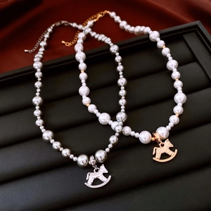 Detail of gold and silver rocking horse pendants on layered pearl necklaces