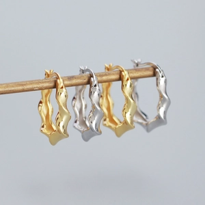 Detailed close-up of wavy geometric hoop earrings in polished gold and silver finishes