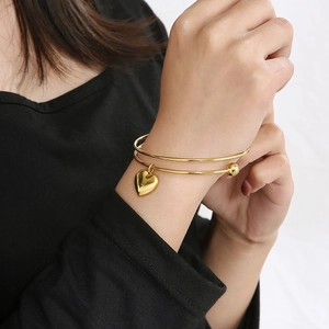 Detailed view of a gold double-layer stainless steel bangle with a heart charm on wrist