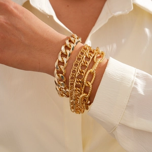Detail view of stacked gold chain bracelets with Cuban and Figaro links on a wrist