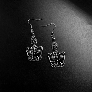 Gothic silver earrings featuring detailed butterfly and skull wings on a dark backdrop