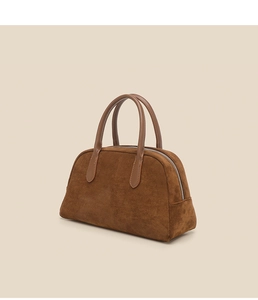 Close-up of brown suede bowling bag featuring smooth leather handles and top zipper detail
