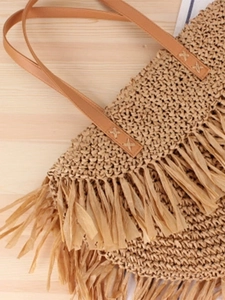Minimalist straw woven tote bag with tassel trim and brown handles for beach vacations